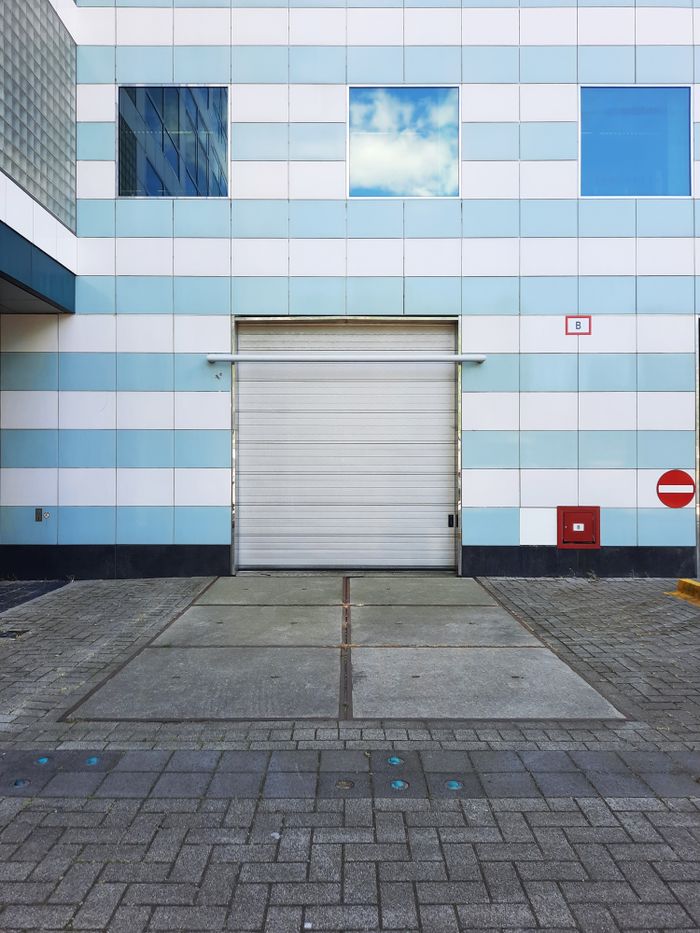 Photo of a warehouse entrance with a closed roller door, showcasing geometric architecture.